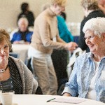 A seated woman smiles at the camera, while another woman smiles at her